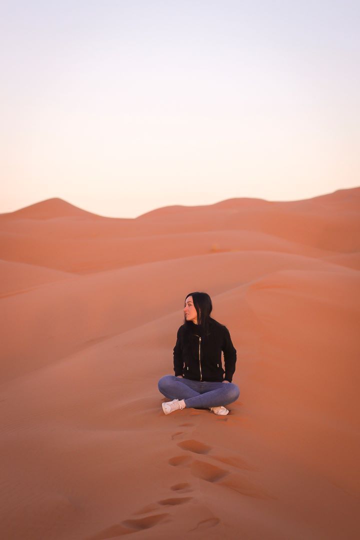 chica sentada con piernas cruzadas mirando al lado izquierdo en la dunas del desierto en marruecos